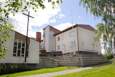Hautauspalveluiden toimisto Iisalmen seurakuntatalo puiston puolelta nähtynä, valkea rakennus josta sisäänkäynti seurakuntasaliin.
